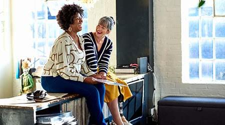 Two women sitting on top of a sideboard laughing